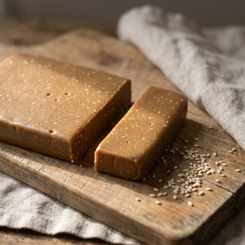 Turrón de ajonjolí partido sobre tabla de madera con ajonjolí suelto